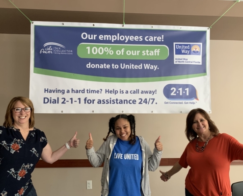 Three Tax Collector Employees standing under United Way banner.
