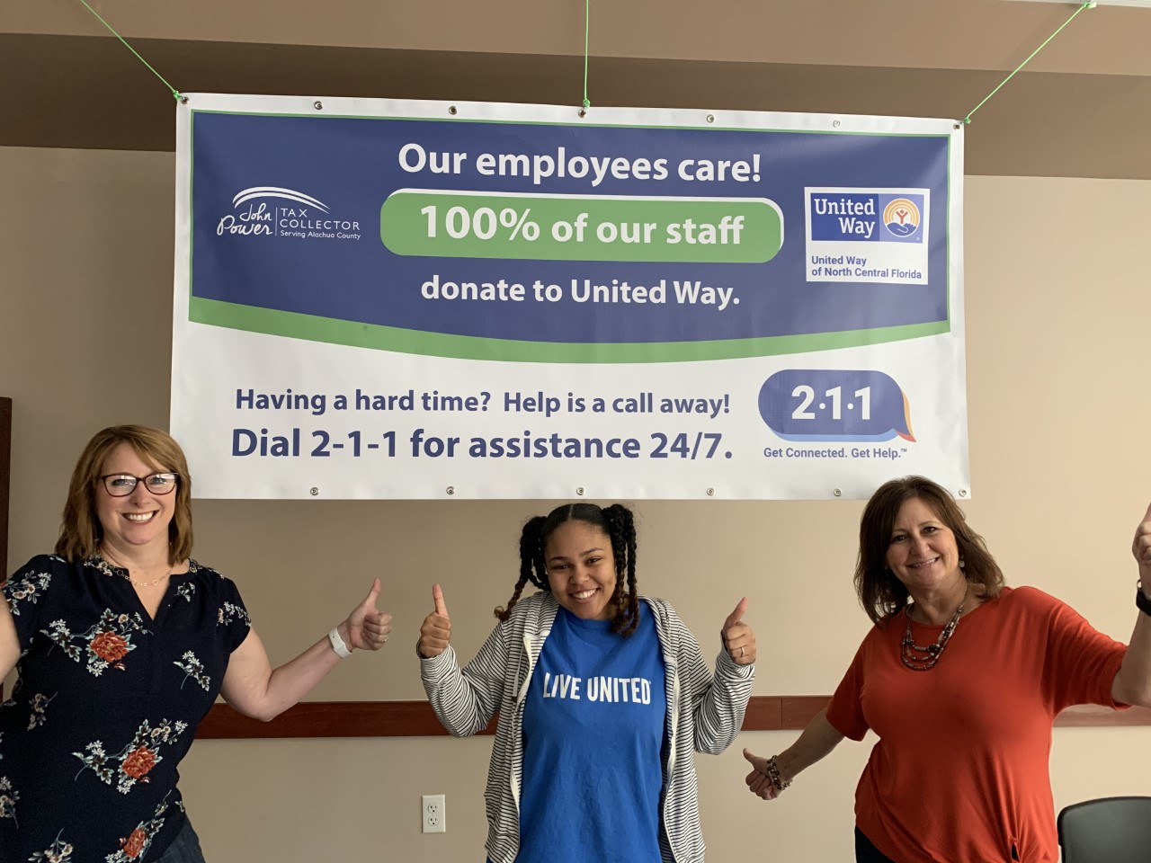 Three Tax Collector Employees standing under United Way banner.